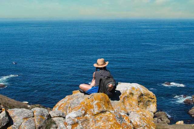 Person sitting on boulder overlooking the ocean