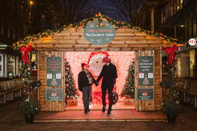 young couple standing in front of a wooden chalet at the swansea christmas market