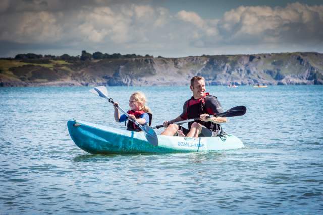 Dad and daughter kayaking on the sea with cliffs in distance on Gower.