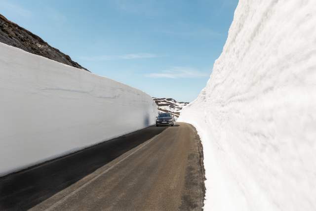 Bil kjører blandt 3 meter høye brøytekanter av snø på Suleskarveien
