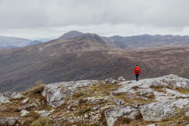 Kvinne i rød jakke på Hovdenuten i Hovden med fjell i bakgrunnen
