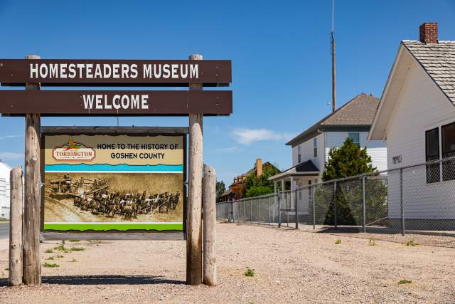 Wooden welcome sign for the Homesteaders Museum in Torrington, Wyoming, featuring historic artwork and homes in the background.