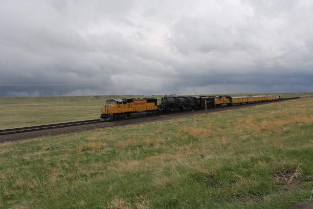 The Union Pacific Big Boy 4014 steam locomotive pulling passenger cars across grassy plains under stormy skies in Wyoming.