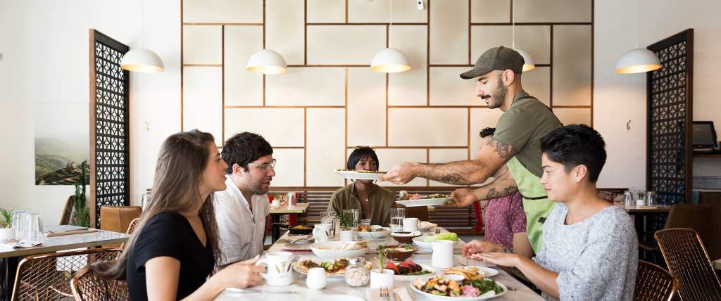 Man Serving Food To 3 People At A Table In Laziz Kitchen