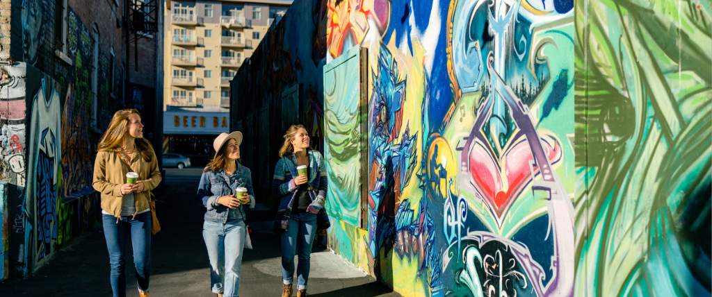 3 girls walking in sunlit alley with murals