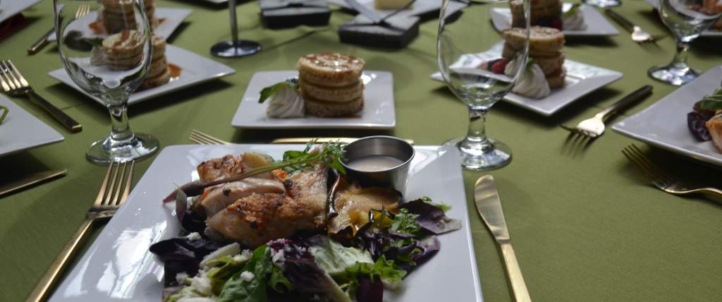 Chicken salad on square plates set on a green table cloth with utensils and dessert