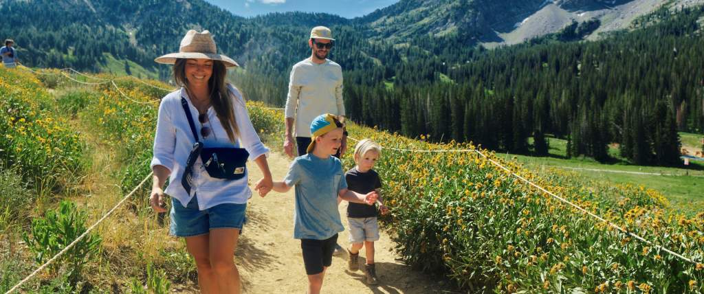 Family Hiking on a trail with wildflowers on each side and the mountains in the background