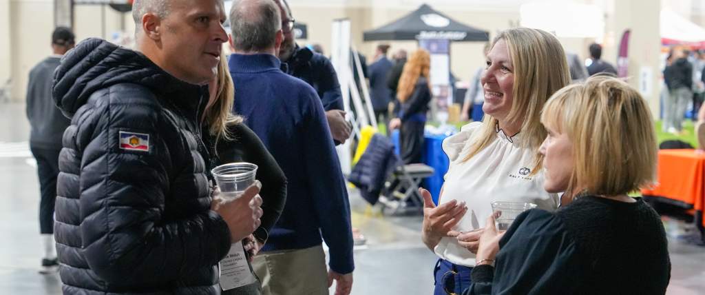 3 smiling people socializing with sports activities and booths in the background