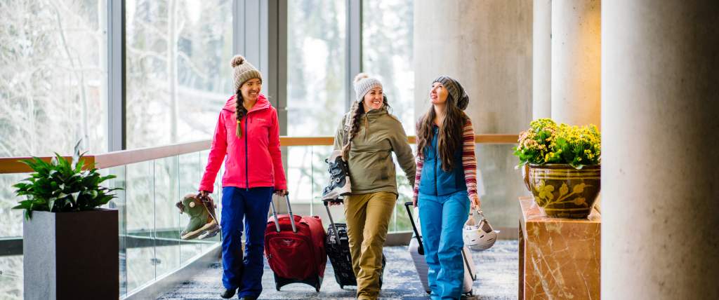 3 women in ski gear pulling suitcases in the atrium area of the Cliff Lodge