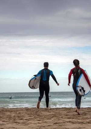 Four surfers running towards the sea to go Surfing at Whiterocks Beach, Portrush, County Antrim