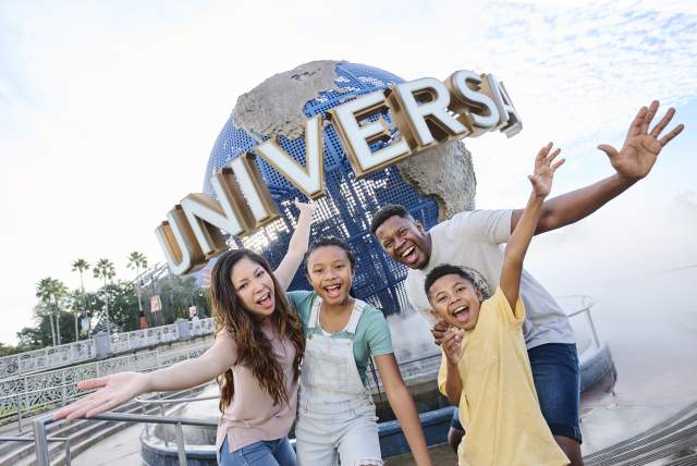 A group of visitors poses with arms raised at the UNIVERSAL globe landmark near the park entrance.