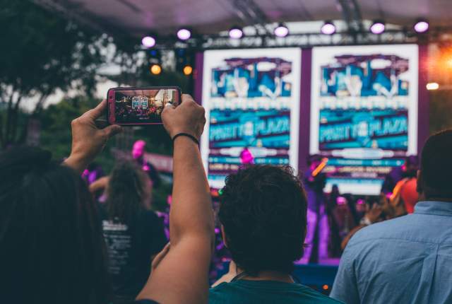A person recording a show with his cell phone in the middle of a crowd