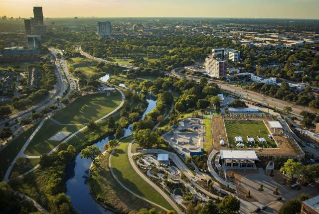 Memorial Drive Dusk. Vista aérea del parque y senderos junto al río en Midtown Houston, con áreas verdes, puentes y edificios rodeados de un paisaje urbano vibrante.