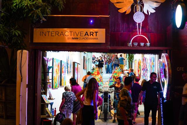 Gente entrando a la galería de Ivan Guaderrama en una noche iluminada, admirando el arte interactivo.