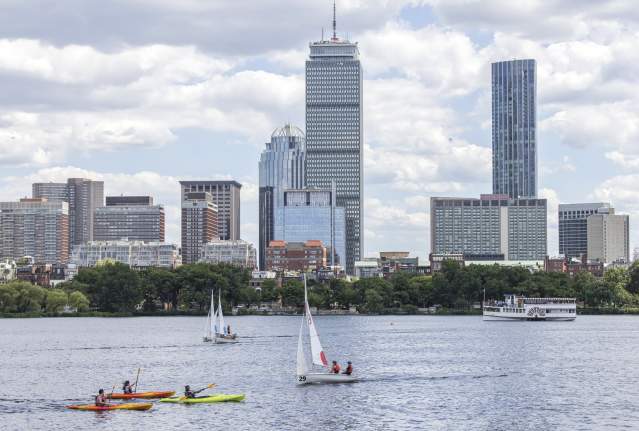 A few kayaks and sailboats on the Charles River with the Boston skyline in the background