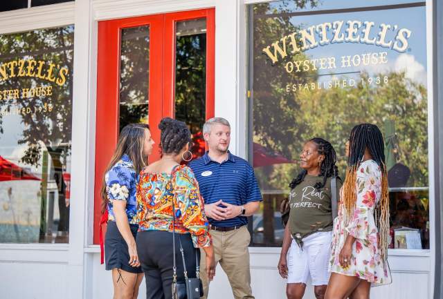 A male tour guide stands outside Wintzell's Oyster House with four female tourists