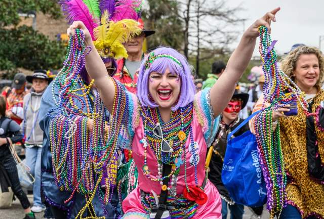 Woman in Mardi Gras costume holding beads and smiling