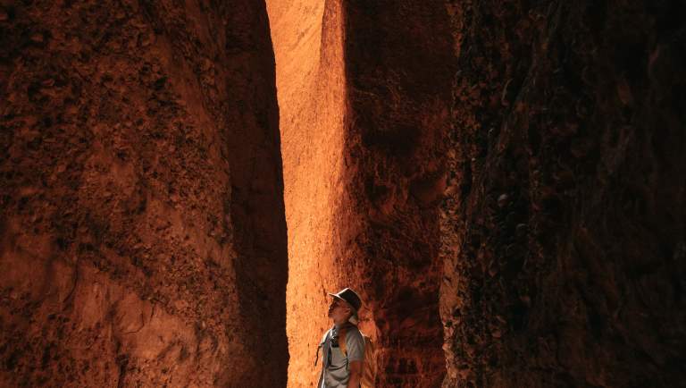 Daylight shines on a man standing in the gap at Echidna Chasm, in Purnululu National Park