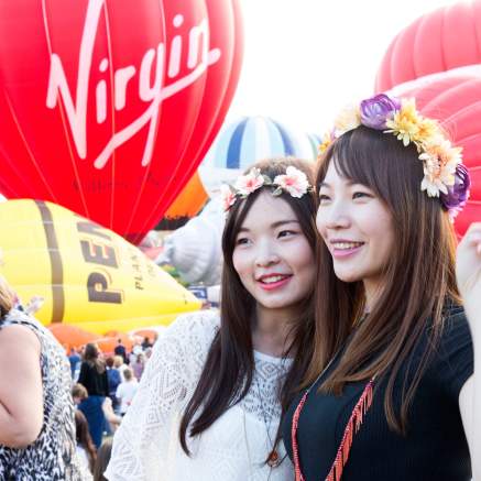 Two women wearing flower crowns standing in front of ascending balloons at Bristol International Balloon Fiesta - credit Paul Box