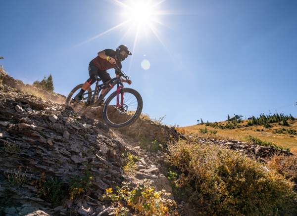 Mountain biker descending rocky trail under bright sun at Brian Head with scenic alpine landscape