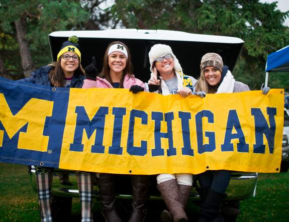 Four women smiling at holding a U-M banner