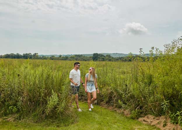 Two people walking in an open field with blue skies above them.
