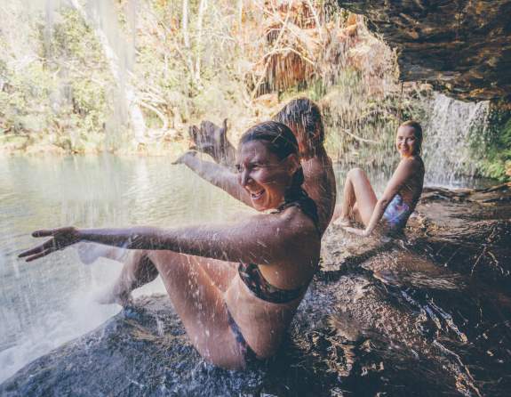 Three people sitting under the waterfalls at Fern Pool in Karijini National Park