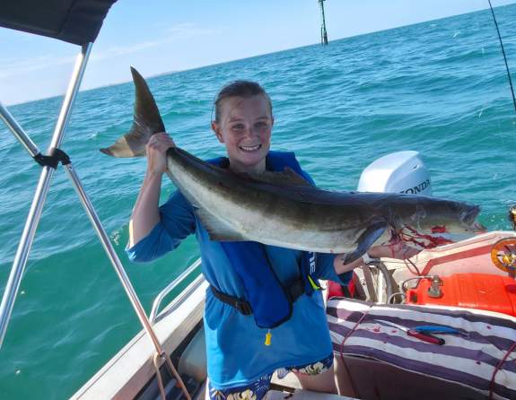 A woman in a boat holding a freshly caught cobia fish, in the waters off Port Hedland
