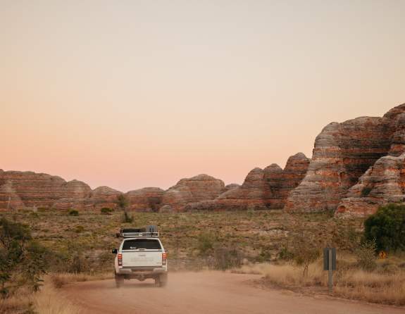 Car driving on unsealed road through the striped domes of the Bungle Bungle Range in Purnululu National Park
