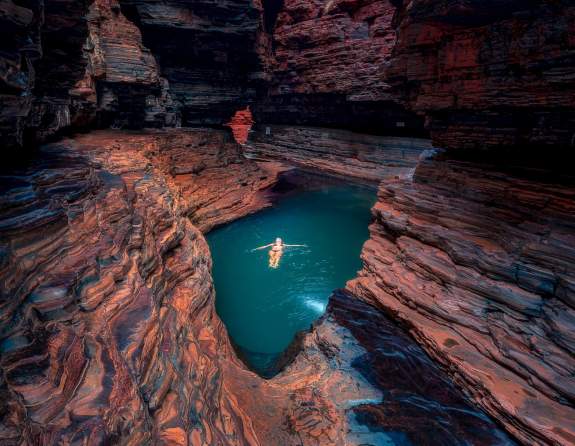 A woman floats in the emerald waters of Kermits Pool, with the walls of Hancock Gorge towering above her.
