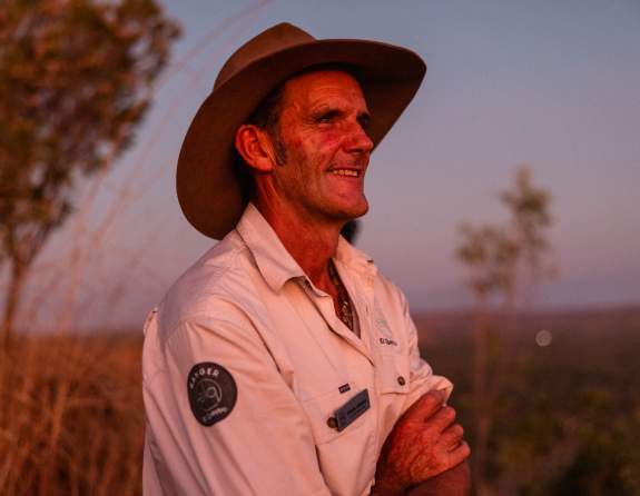 One of El Questro's Rangers wearing an Akubra hat and El Questro shirt standing at sunset