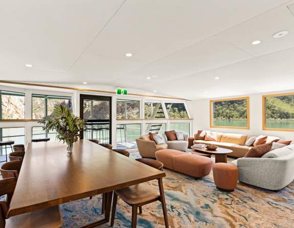 Lounge area of the Jetwave Pearl at the Horizontal Falls, showing comfortable lounge seating, dining table and chairs and views through the windows and balcony area