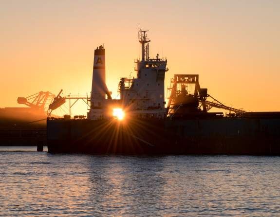 Sun setting behind large ships in port at the Port of Port Hedland