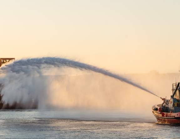 A tugboat spraying water across to a ship in the Port of Port Hedland