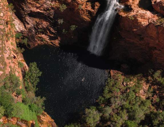Aerial view of a waterfall in El Questro and the freshwater pool beneath it; a person is seen swimming in the water.