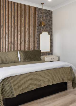 A modern hotel room with a wooden slat wall, a desk, and green bedding.