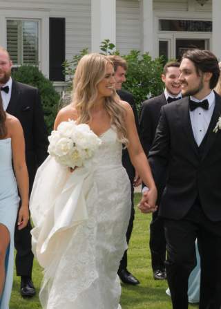 A wedding party walks and smiles in front of a Classic Home at Camelot Manor wedding venue.