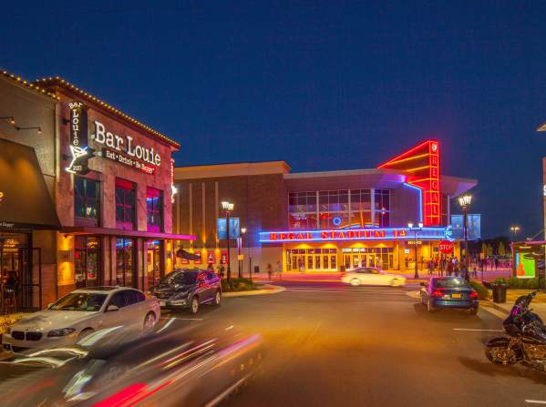 A shopping area at night with neon lights and cars going by