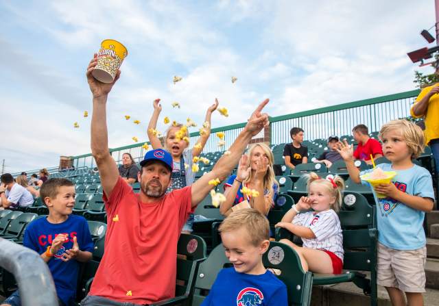 Fans at an Iowa Cubs game throwing popcorn in the air and cheering