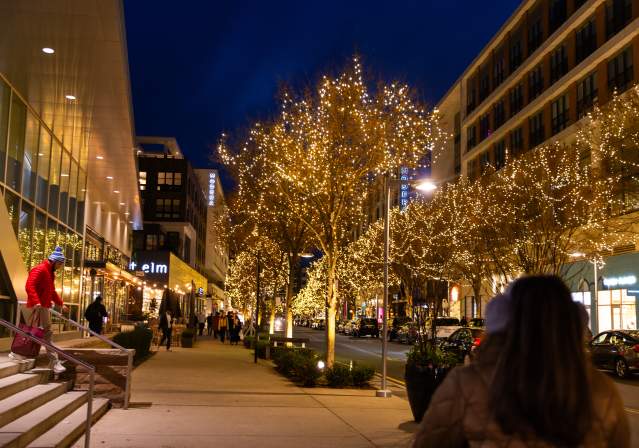 Mosaic District in winter with streets adorned in holiday lights and people walking along a sidewalk at night