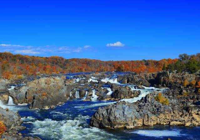 A scenic view of a rocky river with cascading waterfalls, surrounded by autumn foliage and a clear blue sky. Ideal for nature exploration.