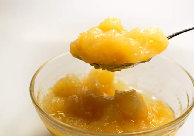 small glass cup willed with applesauce and a spoon dipping into it