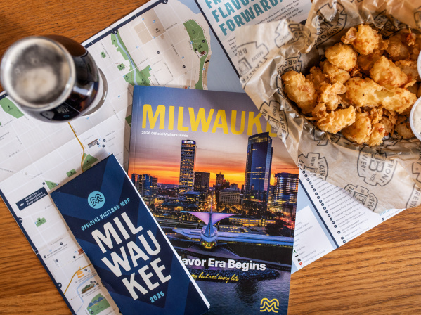 The 2026 Milwaukee Official Visitors Guide and Official Visitors Map are displayed with a beer and cheese curds on a table.