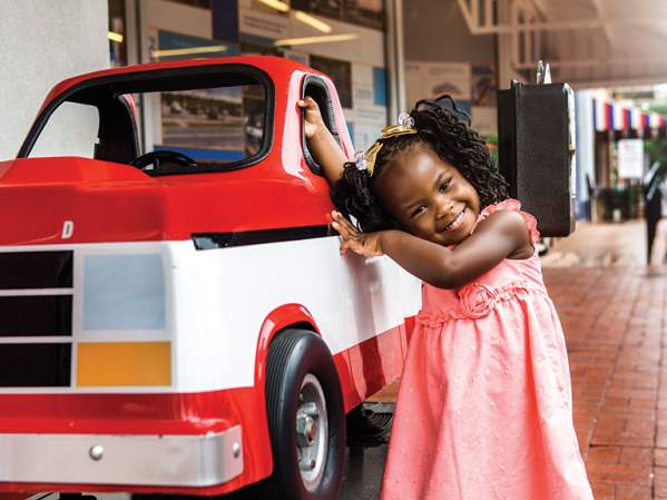 Image of a happy young girl leaning against a a coin operated replica of Sam Walton's truck