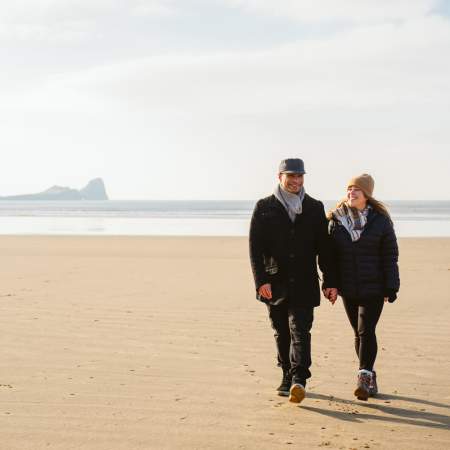 A couple walking on Rhossili beach in the winter.