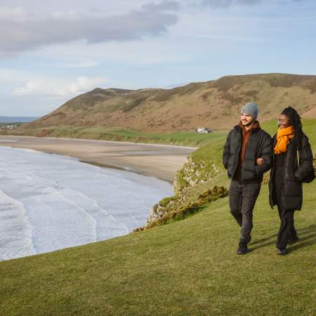 Couple walking along rhossili bay coastline