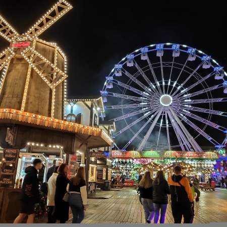 customers walking past stalls and big wheel at winter wonderland