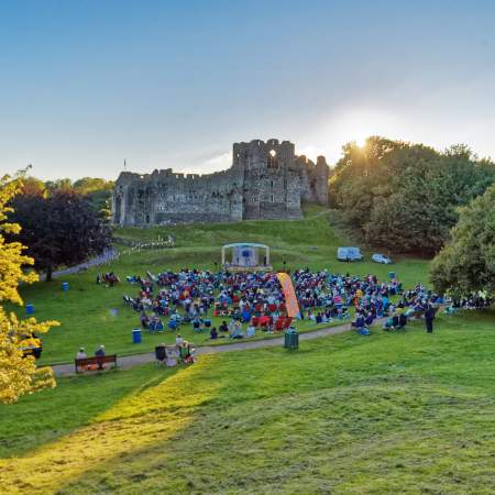 theatre performance with crowd watching on with oystermouth castle in the background at sunset