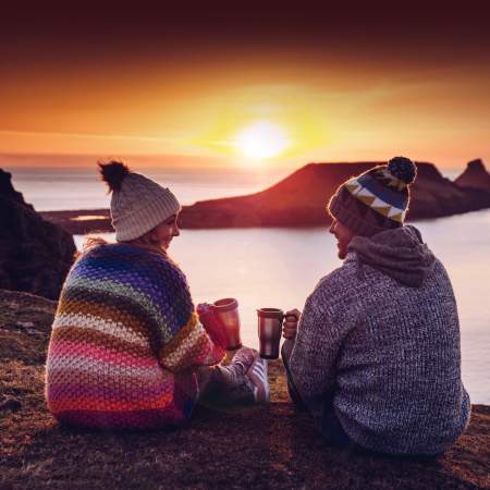 a couple share coffee while the sun sets against worms head