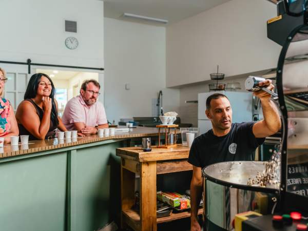 Elio roasting coffee as experience attendees view from the counter and sip on coffee